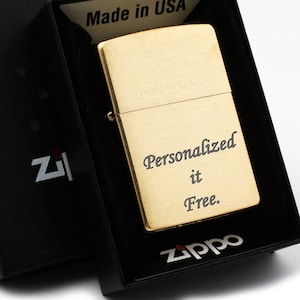 May include: Gold Zippo lighter in a black box. The lighter has the words "Solid Brass" and "Personalized it Free." engraved on it.