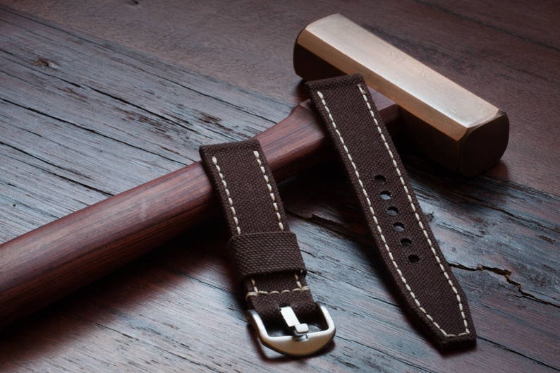 May include: Two brown canvas watch straps with white stitching. One strap has a buckle and the other has a series of holes for adjusting the fit.
