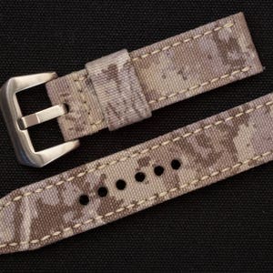 May include: A beige and brown camouflage watch strap with a silver buckle.