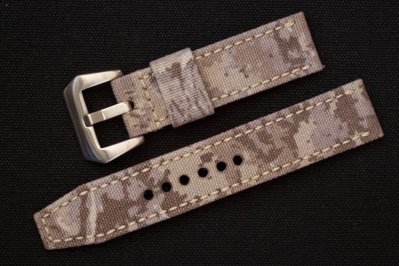 May include: A beige and brown camouflage watch strap with a silver buckle.