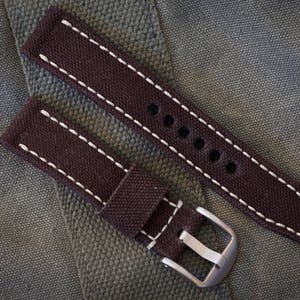 May include: Two brown canvas watch straps with white stitching. The straps have metal buckles and are designed for a wristwatch.