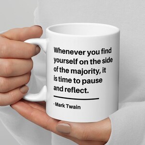Puede incluir: Taza de cerámica blanca con una cita en negro de Mark Twain: "Siempre que te encuentres del lado de la mayoría, es hora de hacer una pausa y reflexionar."