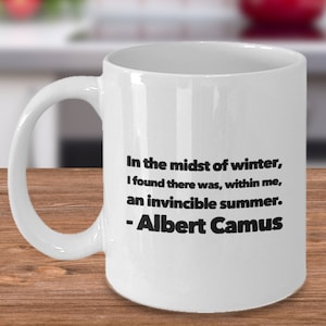 May include: White ceramic coffee mug with a black quote by Albert Camus: "In the midst of winter, I found there was, within me, an invincible summer."
