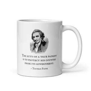 K&ouml;nnte beinhalten: Wei&szlig;e Keramik-Tasse mit einem Schwarz-Wei&szlig;-Portr&auml;t von Thomas Paine und einem Zitat. Das Zitat lautet: "Die Pflicht eines wahren Patrioten ist es, sein Land vor seiner Regierung zu sch&uuml;tzen."