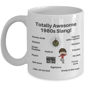 May include: White ceramic coffee mug with a black design featuring 1980s slang terms and illustrations, including a disco ball, a boombox, and a person with a big afro.