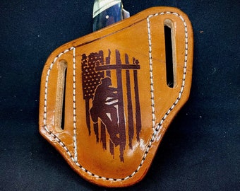 May include: A brown leather knife sheath with a white stitched border. The sheath has an American flag design with a silhouette of a person climbing a utility pole.