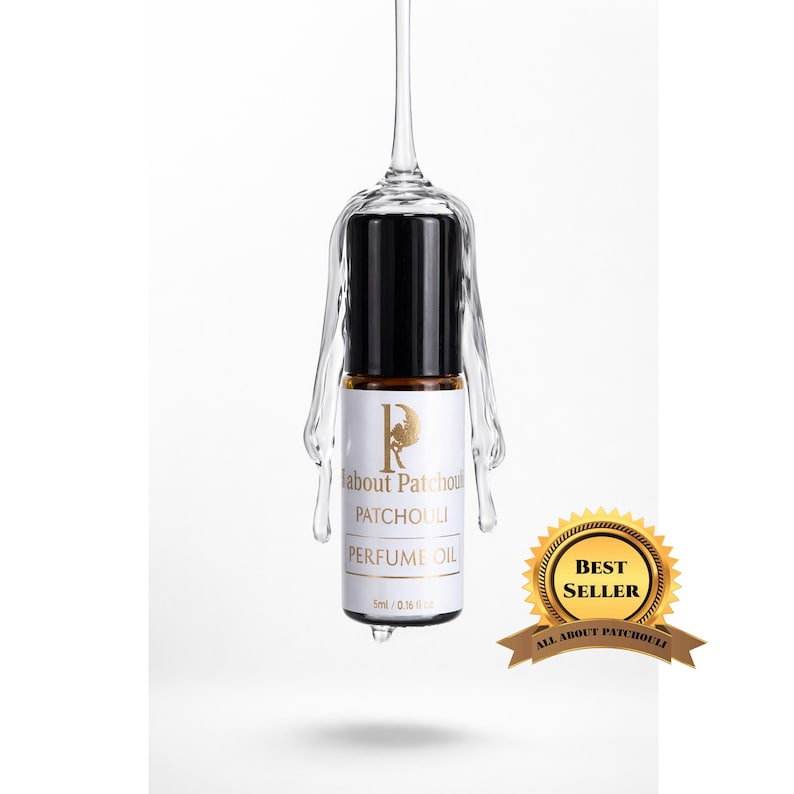 May include: A perfume oil bottle with a black cap and a white label featuring the text "Patchouli Perfume Oil". The bottle is suspended in a clear glass holder. A gold "Best Seller" seal is visible.