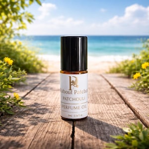 May include: A perfume oil bottle with a black cap and a white label. The label reads "About Patchouli PERFUME OIL" with a gold logo. The bottle contains 0.16 fl oz of perfume oil. The background shows a beach scene.