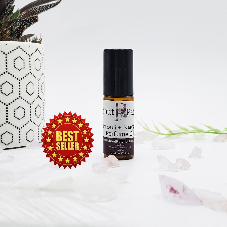May include: A small perfume oil bottle with a black cap and a label that reads "houli + Nag Perfume Oil." The bottle is brown and sits next to a "Best Seller" sticker. The bottle contains 0.17 fl oz of perfume oil.