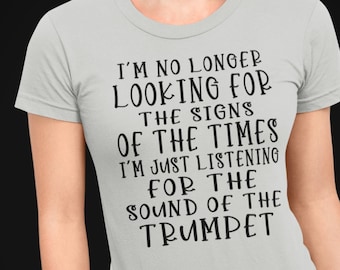 May include: A light gray t-shirt with the text "I'M NO LONGER LOOKING FOR THE SIGNS OF THE TIMES I'M JUST LISTENING FOR THE SOUND OF THE TRUMPET" in black. The shirt is short-sleeved.