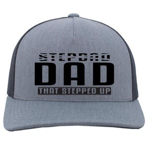 May include: A gray trucker hat with a black mesh back. The front of the hat features the words "STEPDAD DAD THAT STEPPED UP" in bold, black letters. The hat has a curved brim and a snapback closure.