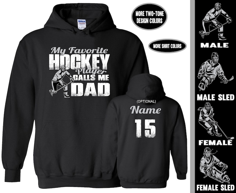 May include: Black hooded sweatshirt with a white graphic that says "My Favourite Hockey Player Calls Me Dad". The graphic includes a hockey player with a stick and puck. The back of the sweatshirt has a white graphic with the word "Name" and the number "15".