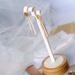 Pode incluir: Um par de brincos de ouro com um design circular e uma corrente de pérolas brancas penduradas.