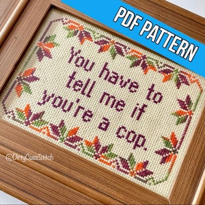 Puede incluir: Patrón de punto de cruz en un marco de madera. El texto dice: "You have to tell me if you're a cop." El diseño presenta un borde de hojas en tonos naranja, verde y burdeos. Las palabras están bordadas en color púrpura oscuro.