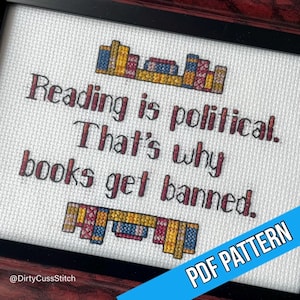 May include: Cross-stitch art in a black frame with the text "Reading is political. That's why books get banned." The design includes stitched book graphics and a blue PDF PATTERN banner.