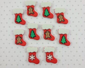 May include: A collection of red Christmas stocking-shaped embellishments with white fur trim. Some stockings feature a green Christmas tree, a gingerbread man, or a white snowflake. The background is a light gray dotted pattern.