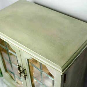 K&ouml;nnte beinhalten: Eine gr&uuml;ne Holzk&auml;stchen f&uuml;r Schmuck mit Glast&uuml;ren und einem dekorativen Rand. Die Box hat eine abgenutzte Oberfl&auml;che und ist geschlossen.