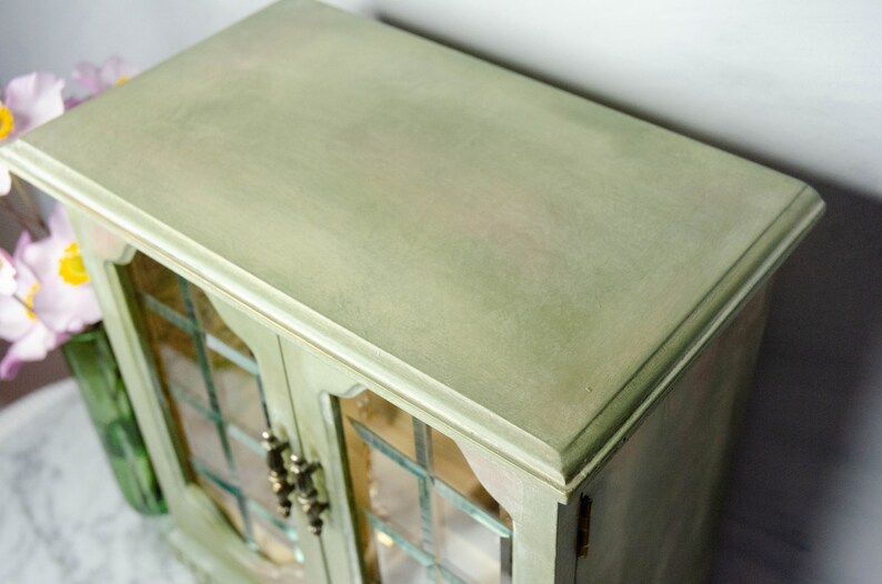 K&ouml;nnte beinhalten: Eine gr&uuml;ne Holzk&auml;stchen f&uuml;r Schmuck mit Glast&uuml;ren und einem dekorativen Rand. Die Box hat eine abgenutzte Oberfl&auml;che und ist geschlossen.