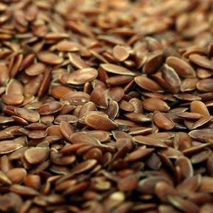 May include: Close-up of a pile of brown flax seeds. The seeds are oval-shaped and have a smooth, shiny texture. The image is well-lit, showing the details of each seed. The seeds are scattered, creating a natural and organic feel.