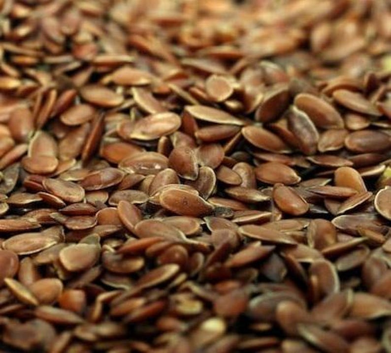 May include: Close-up of a pile of brown flax seeds. The seeds are oval-shaped and have a smooth, shiny texture. The image is well-lit, showing the details of each seed. The seeds are scattered, creating a natural and organic feel.