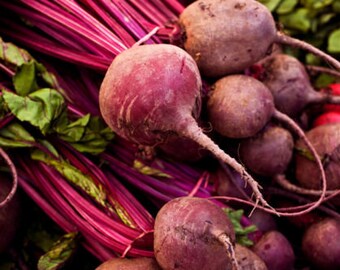May include: A close-up shot of freshly harvested beets. The image showcases a vibrant display of deep red beetroots with their attached stems and green leaves. The beets vary in size and shape, with visible soil clinging to their surfaces.