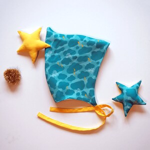 May include: A turquoise blue fabric hat with a white and yellow cloud and lightning bolt pattern. The hat has yellow ties and comes with two yellow fabric stars.