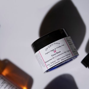 May include: A black jar with a blue lid labeled "The Gypsy Forest Organic Vegan & Cruelty Free Coco Rose Moisturizer All | Combination Skin Types Acne - Redness - Inflammation Hydrate - Soften & Smooth - Balance Sebum"