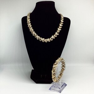 May include: A gold necklace and bracelet set with a heart-shaped design and clear stones. The necklace is displayed on a black velvet stand and the bracelet is on a clear stand.