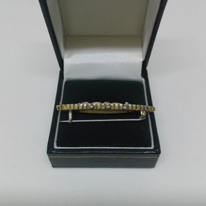 May include: A gold and silver brooch with a geometric design, displayed in a green velvet box.