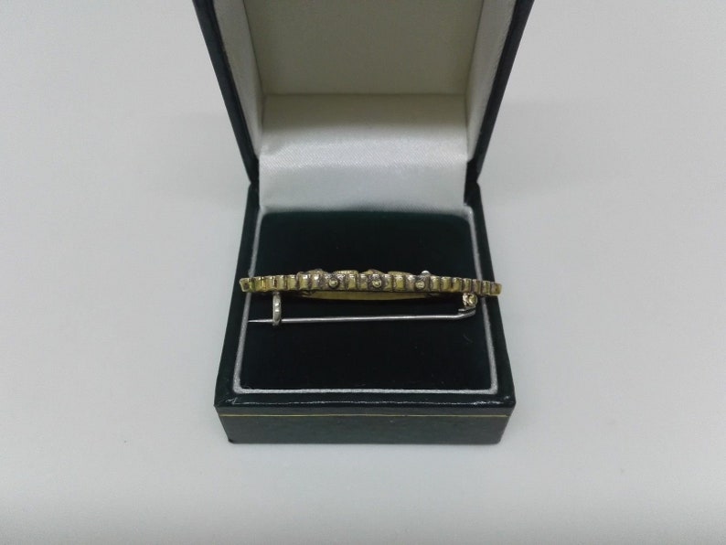 May include: A gold and silver brooch with a geometric design, displayed in a green velvet box.