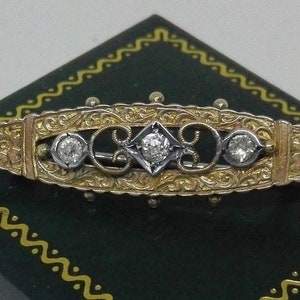 May include: A gold and silver brooch with a delicate floral design and three round diamonds.