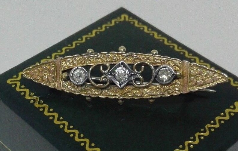 May include: A gold and silver brooch with a delicate floral design and three round diamonds.