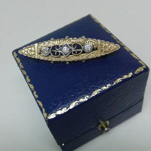 May include: A gold and silver brooch with a delicate floral design and three round diamonds. The brooch is displayed in a blue velvet box.
