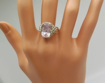 May include: A silver ring featuring a large oval pink gemstone set in a delicate filigree design.