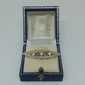 May include: A gold and silver brooch with three diamonds set in a delicate filigree design. The brooch is in a blue velvet box with the inscription "Mappin & Webb London".