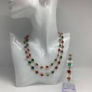 Könnte beinhalten: Ein goldfarbenes Halsketten- und Armband-Set. Die Halskette hat zwei Stränge aus bunten, runden Edelsteinen. Das Armband hat einen einzelnen Strang aus passenden Edelsteinen. Die Edelsteine sind rot, grün, blau und lila.