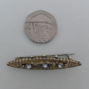 May include: A gold-toned brooch with a decorative design and five clear stones set in the center.