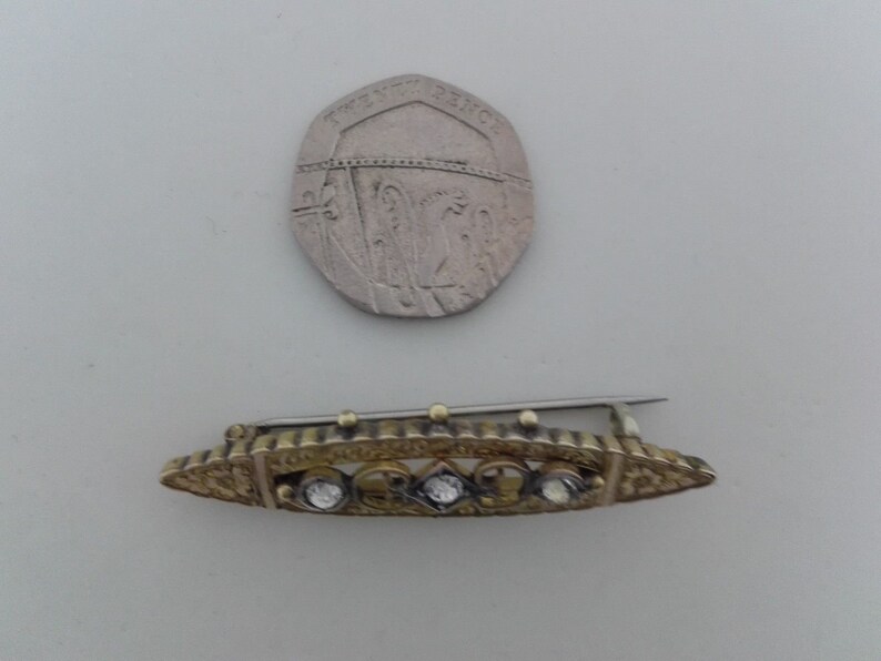 May include: A gold-toned brooch with a decorative design and five clear stones set in the center.