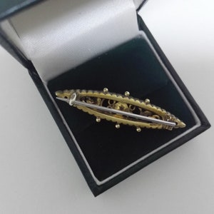 May include: A gold-toned brooch with a delicate design and a pin on the back. The brooch is in a black velvet box.