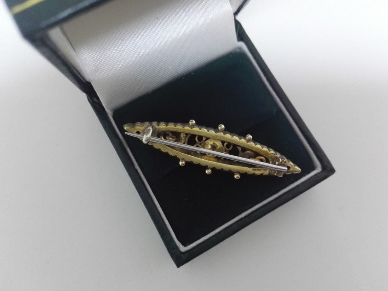 May include: A gold-toned brooch with a delicate design and a pin on the back. The brooch is in a black velvet box.