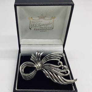 May include: A silver bow brooch in a black velvet box. The box is labeled "Watchmaker & Jeweller T.C. Farrington The Square Edenbridge Kent."