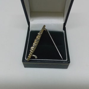 May include: A gold and silver brooch with a decorative design, in a black velvet box.