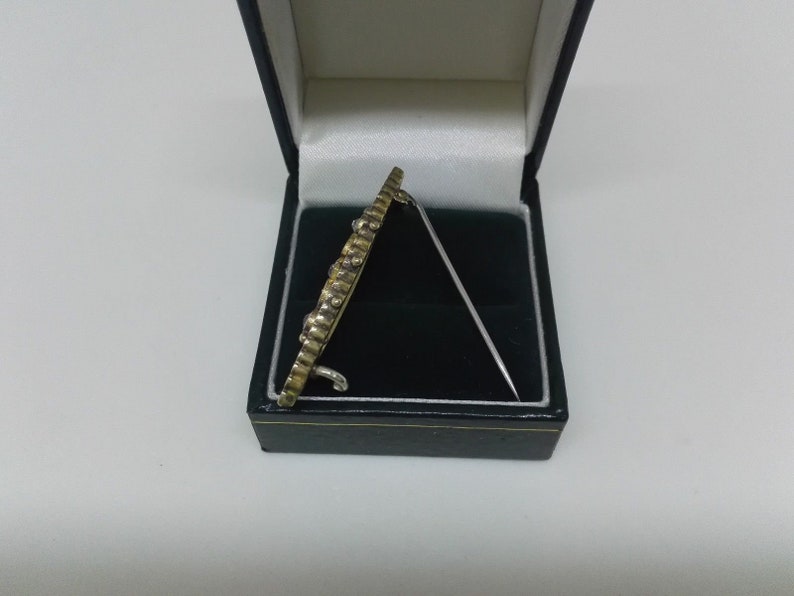 May include: A gold and silver brooch with a decorative design, in a black velvet box.