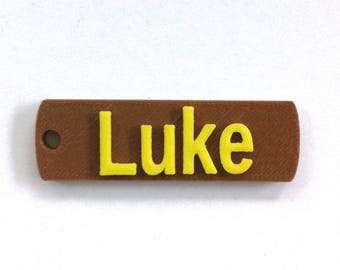 May include: A brown rectangular name tag with a yellow inscription that reads "Luke".