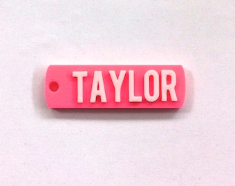 May include: A pink plastic keychain with a white inscription that reads "TAYLOR".