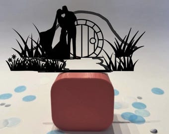 May include: A black silhouette of a couple kissing in front of a round door, with grass and flowers. The silhouette is on top of a red square block. Blue and white confetti dots the white surface.