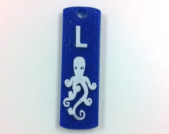 May include: A blue plastic tag with a white octopus and the letter "L" printed on it.
