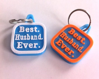 May include: Two blue and white keychains with the text "Best Husband Ever." One keychain has a white border and the other has an orange border.