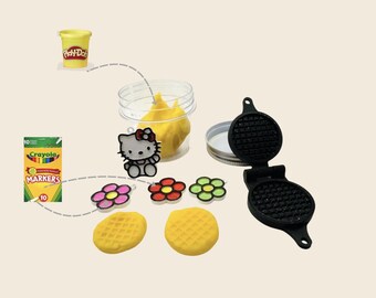 May include: A collection of children's toys and craft supplies, including a Play-Doh container, a box of Crayola markers, and a miniature waffle maker. Also featured are flower-shaped charms, a Hello Kitty charm, and two yellow Play-Doh waffles.