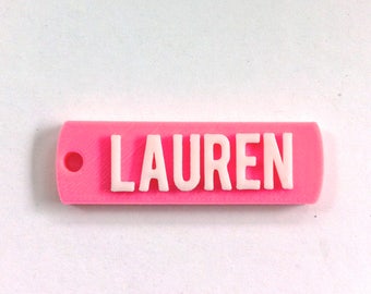 May include: Pink plastic keychain with the name "LAUREN" in white raised letters.